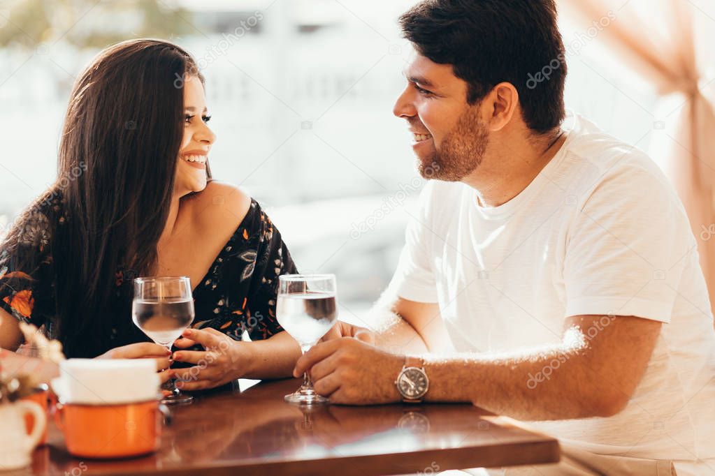 Young couple in love sitting in a cafe, drinking water, having a conversation and enjoying the time spent with each other.