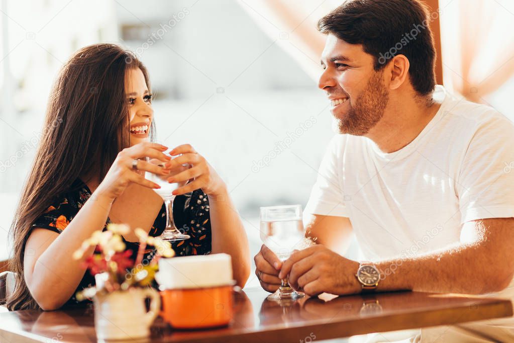 Young couple in love sitting in a cafe, drinking water, having a conversation and enjoying the time spent with each other.