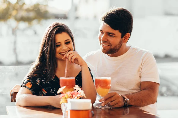 Pasangan muda jatuh cinta duduk di sebuah restoran, minum minuman berwarna-warni, mengobrol dan menikmati waktu yang dihabiskan satu sama lain — Stok Foto