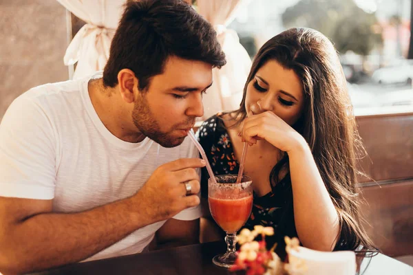 Pareja joven enamorada sentada en un restaurante, bebiendo bebida colorida, conversando y disfrutando del tiempo pasado juntos — Foto de Stock