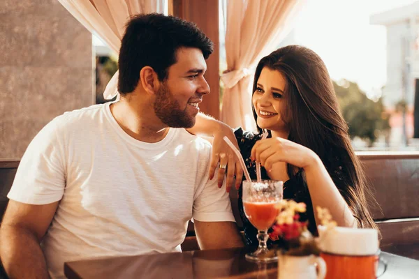 Молода закохана пара сидить у ресторані, п'є барвистий напій, розмовляє і насолоджується часом, проведеним один з одним — стокове фото
