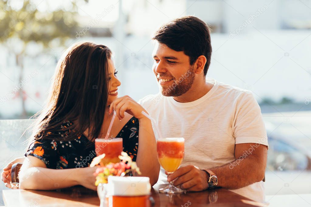 Young couple in love sitting in a restaurant, drinking colorful drink, having a conversation and enjoying the time spent with each other