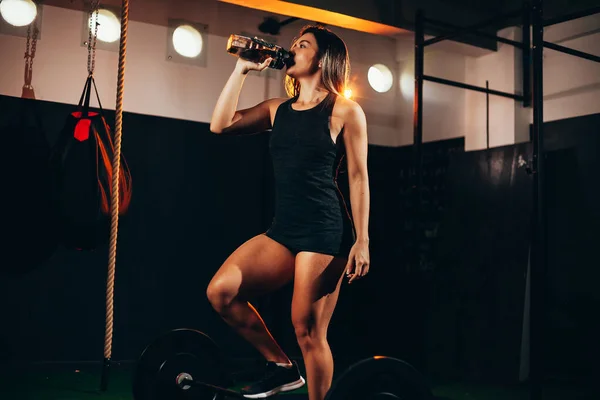 Encaixe a jovem mulher bebendo água no ginásio. Mulher muscular fazendo pausa após o exercício . — Fotografia de Stock