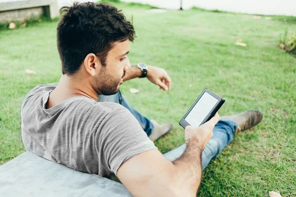 Молодой человек читает электронную книгу в парке — стоковое фото