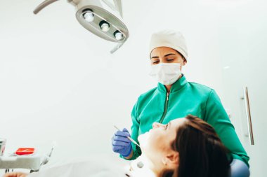 Kadın dişçi kliniğinde bir hastayı muayene ediyor.