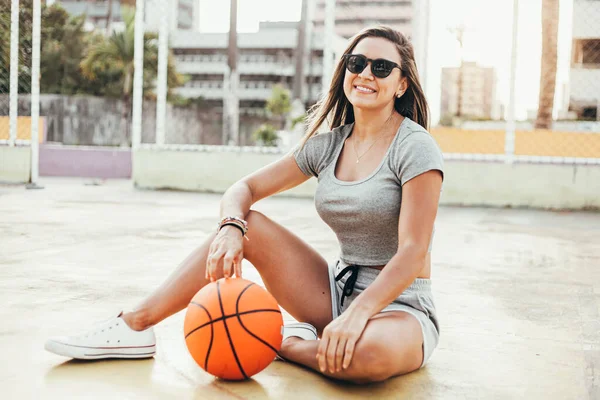 Fitness-Frau entspannt sich nach dem Training sitzend mit einem Basketball. Frau im Fitnessanzug sitzt und entspannt beim Training — Stockfoto