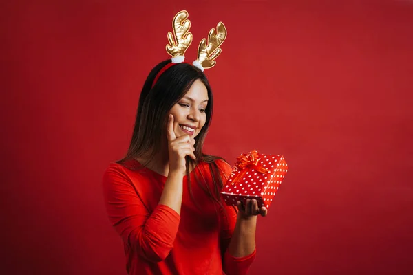 Portrait of thoughtful woman wearing reindeer antlers hat holding gift box