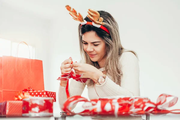 Wanita Natal dengan ikat kepala rusa kutub menyiapkan kertas pembungkus hadiah untuk liburan — Stok Foto