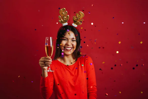 Vacker jul kvinna med champagne glas under konfetti regn över röd bakgrund — Stockfoto