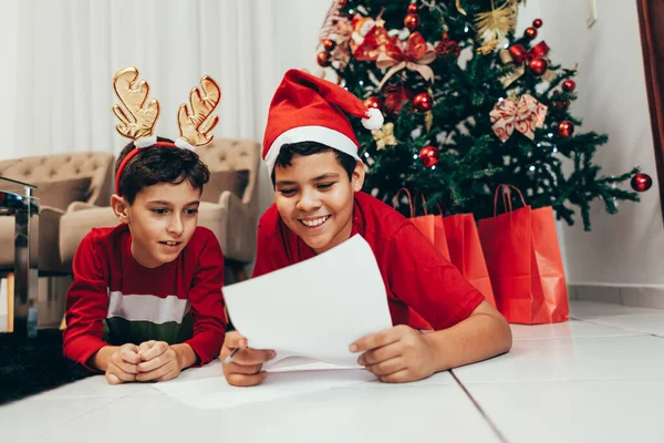 Anak laki-laki berbaring di lantai di bawah pohon Natal menulis daftar keinginan untuk Santa. Menunggu Natal. Perayaan. Tahun Baru . — Stok Foto