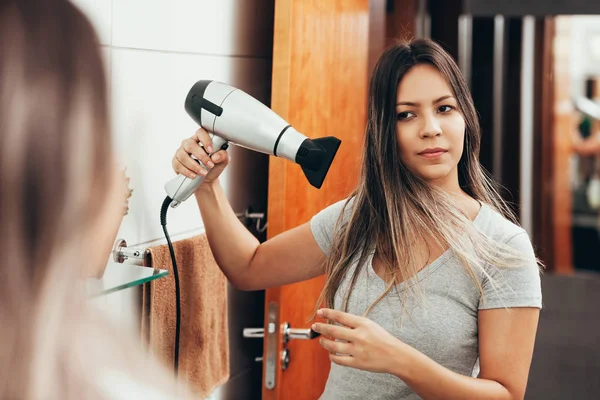 Jonge vrouw met haardroger in de badkamer — Stockfoto