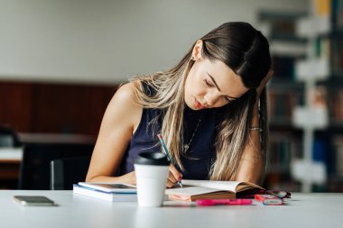 Kütüphanedeki masada okuyan genç bir kadın.