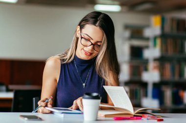 Kütüphanedeki masada okuyan genç bir kadın.