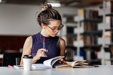 Kütüphanedeki masada okuyan genç bir kadın.