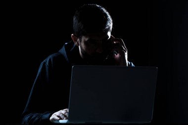 Bilgisayar korsanının karanlık odada bilgisayar ve akıllı telefon kullanarak dramatik görüntüsü.