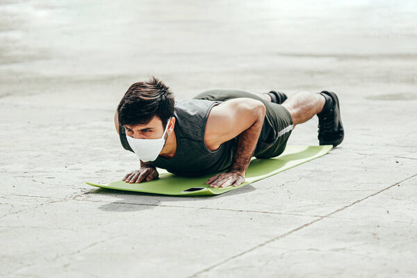 Young man working out outdoors wearing protective mask. Covid-19 and coronavirus concept