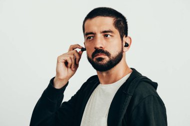 Young bearded man wearing sports clothes putting on wireless earphones. clipart