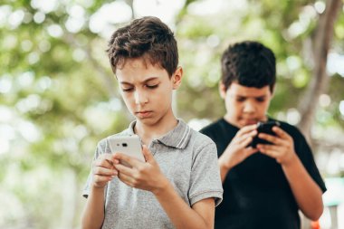 Dışarıda cep telefonu kullanan iki çocuk. Akıllı telefondan video oyunu oynayan çocuklar.