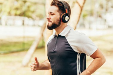 Spor giyimli ve kulaklık takan bir adam parkta tek başına koşuyor.