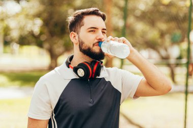 Spor kıyafeti giyen ve kulaklık takan bir adam egzersize ara verdiğinde su içiyor..