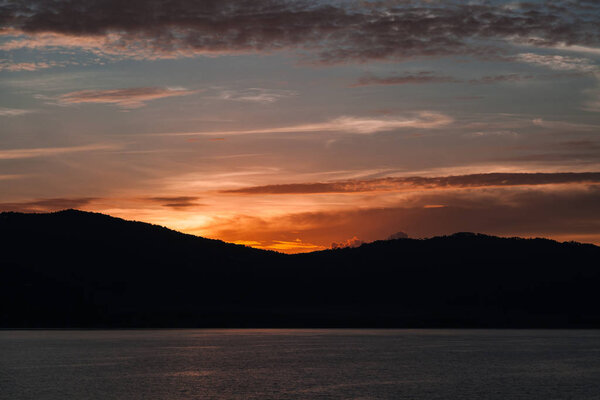 beautiful sunset over silhouette of hills and water surface