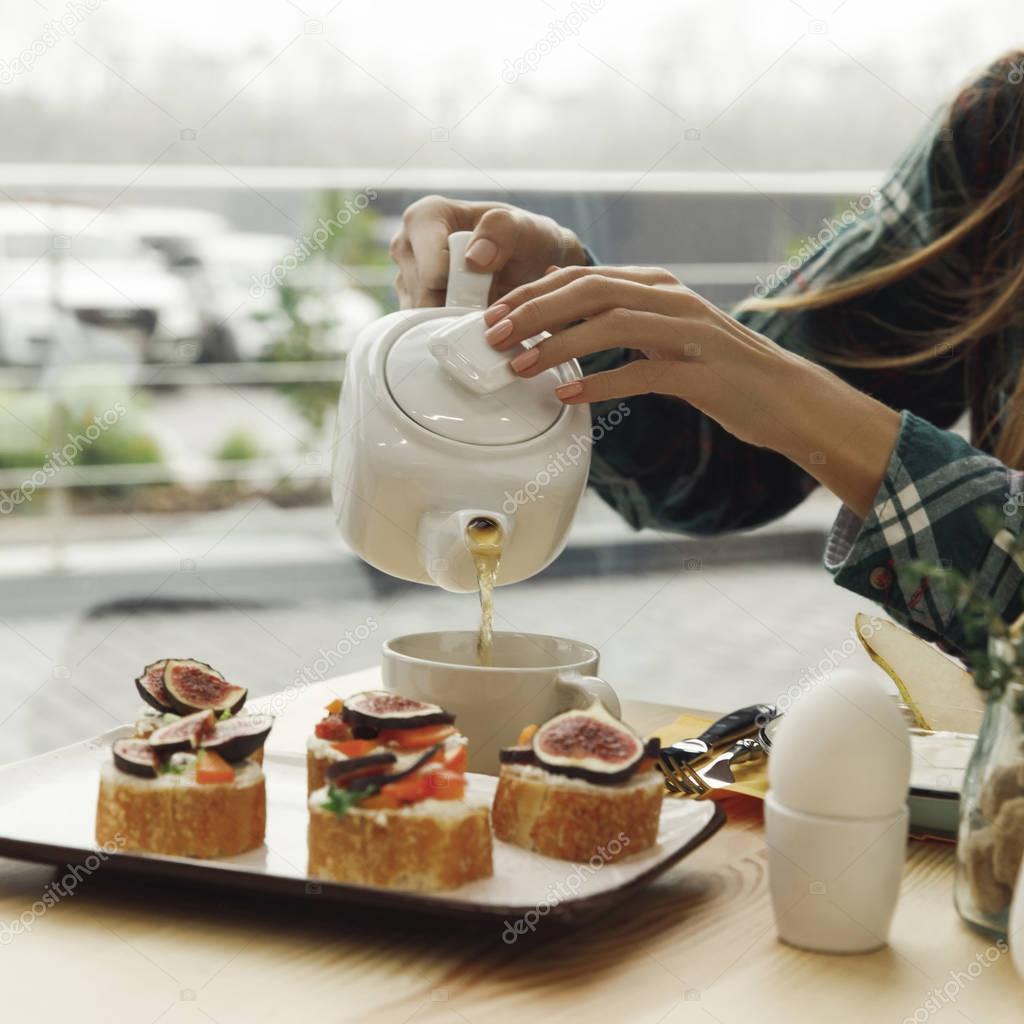 cropped shot of girl pouring tea from teapot while having breakfast  