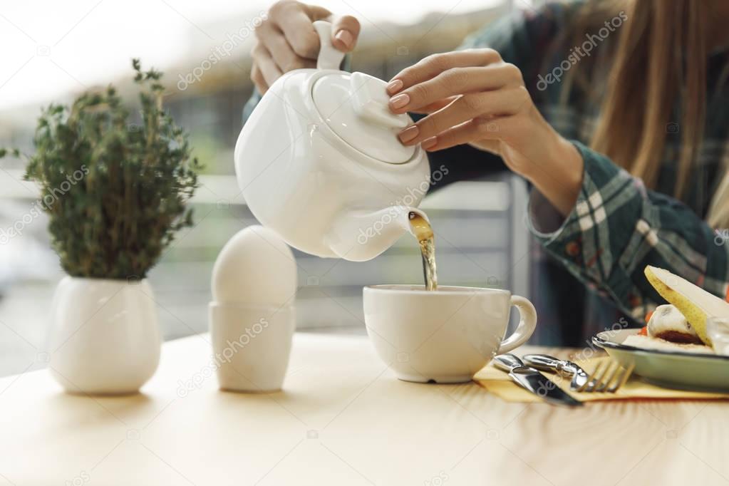 partial view of girl pouring tea from teapot in cup at breakfast 