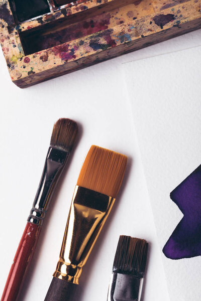 top view of watercolor paints and paintbrushes with drawing album at designer workplace 