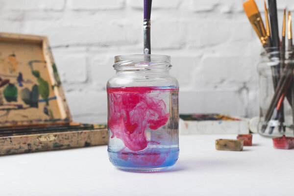 close-up view of glass jar with water and paint at designer workplace