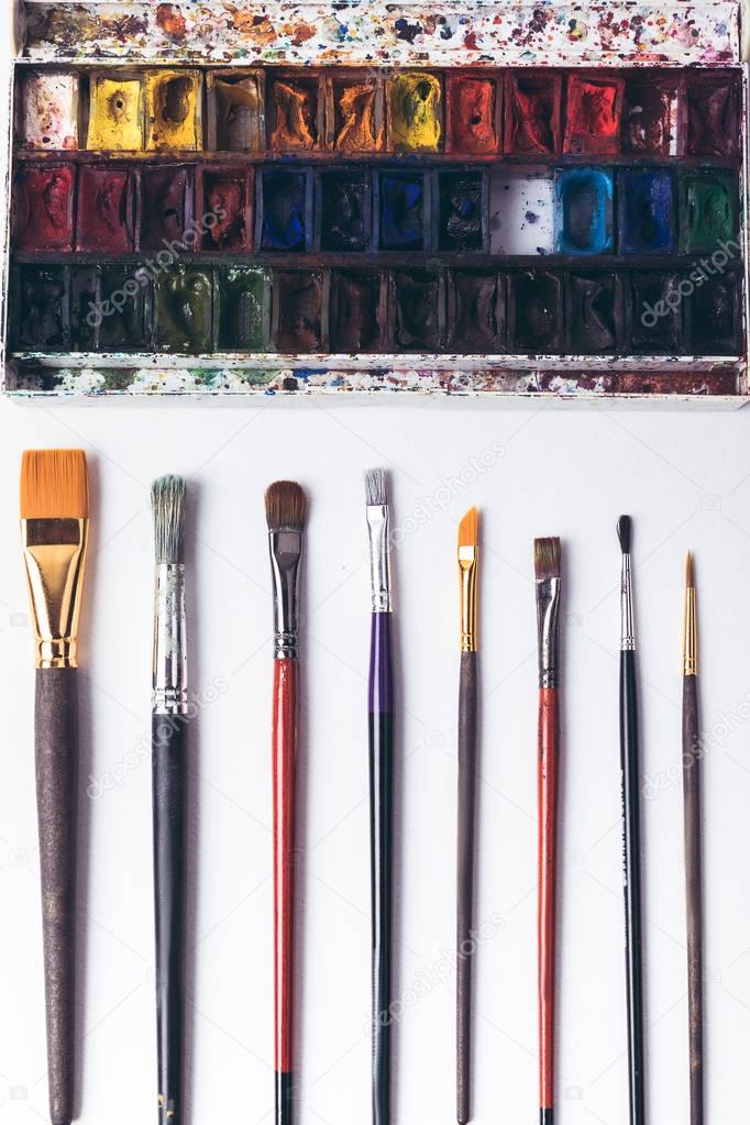 top view of well ordered paintbrushes and watercolour paints at designer workplace  