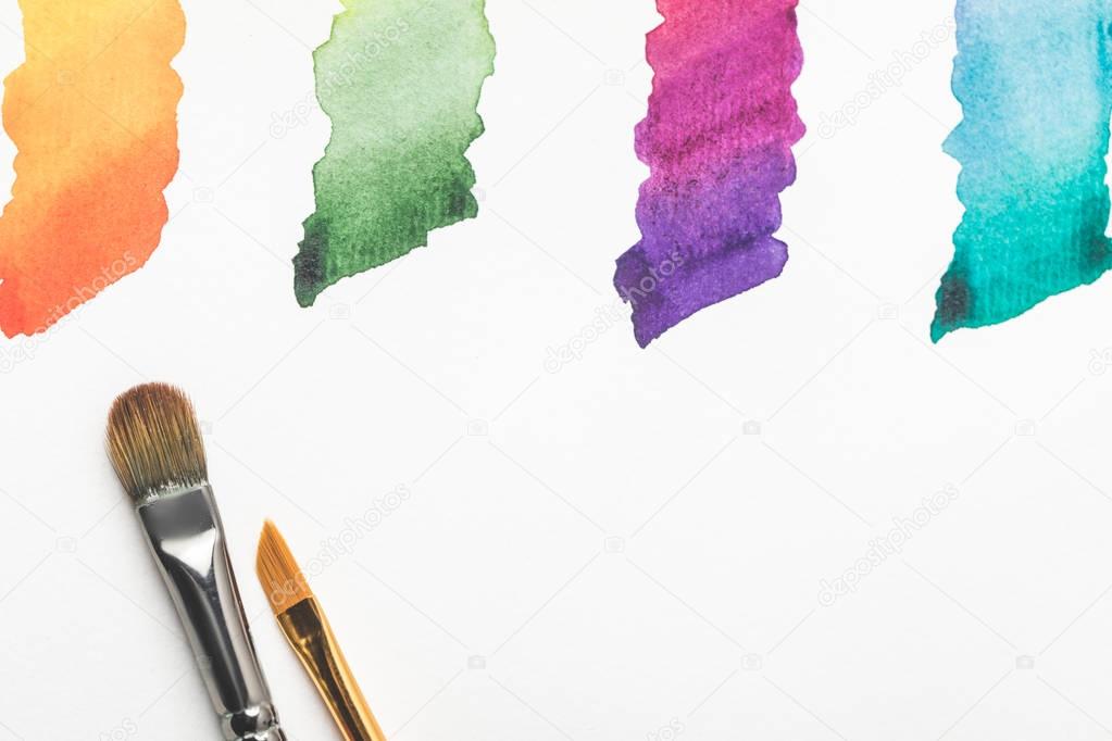 close-up view of paintbrushes and colorful bright paint strokes isolated on white