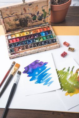 top view of paints, paintbrushes and watercolor sketches at designer workplace clipart