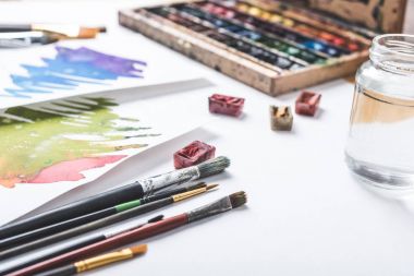 close-up view of paints, paintbrushes and watercolor sketches at designer workplace  clipart