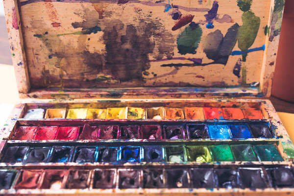 Крупный план акварельных красок в грязном контейнере с мазками и пятнами
