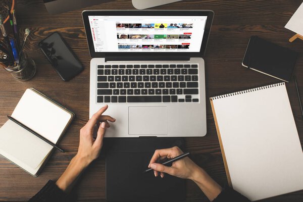 обрезанный снимок дизайнера с помощью графического планшета и ноутбука с сайта YouTube на экране
 