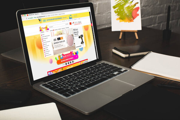 close-up view of designer workplace with notebooks and laptop with aliexpress website on screen