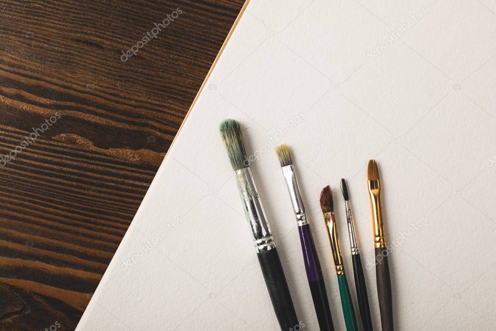 top view of paint brushes and blank drawing album on wooden table 