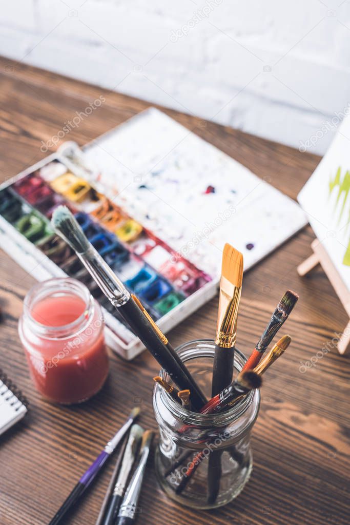 selective focus of watercolor paints and paintbrushes at designer workplace