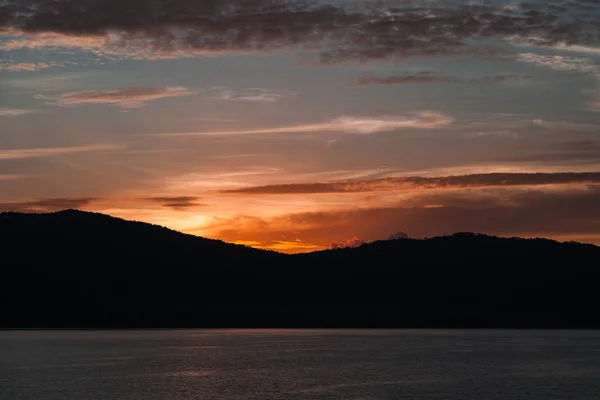 Belo pôr do sol sobre a silhueta de colinas e superfície da água — Fotografia de Stock