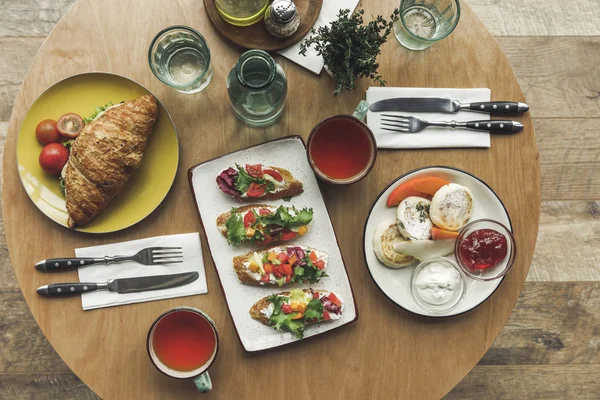 Vista dall'alto di tazze da tè, panini e cheesecake in tavola serviti a colazione — Foto stock