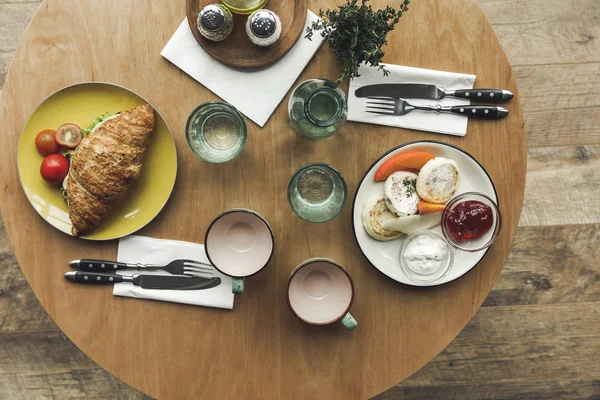 Vista superior de tazas de té vacías, sándwich y tartas de queso en la mesa servido para el desayuno - foto de stock