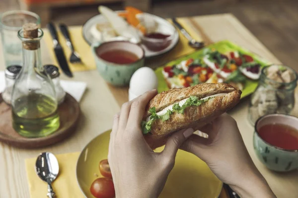 Gros plan vue partielle de la personne qui mange un sandwich savoureux frais au petit déjeuner — Photo de stock
