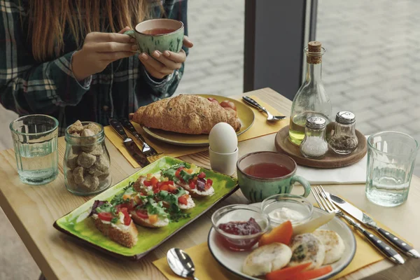 Plan recadré de fille tenant tasse de thé tout en prenant le petit déjeuner — Photo de stock