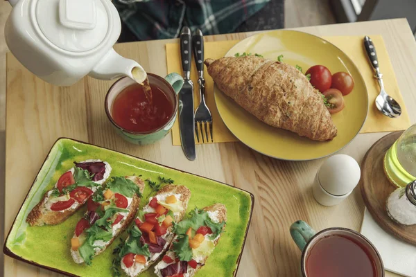 Nahaufnahme von frischen Sandwiches, Croissant und Tee in Tassen zum Frühstück — Stockfoto