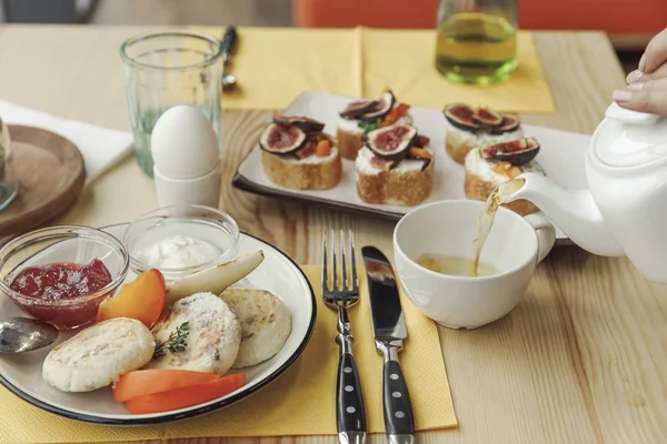 Abgeschnittene Aufnahme von Person, die Tee aus Teekanne und leckeres gesundes Frühstück auf den Tisch gießt — Stockfoto