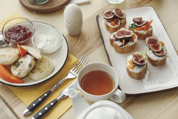 Vista de cerca de sabroso desayuno saludable con buñuelos de tartas de queso y canapés con higos en la mesa - foto de stock