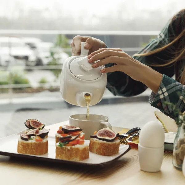 Tiro cortado de menina derramando chá de bule enquanto toma café da manhã — Fotografia de Stock