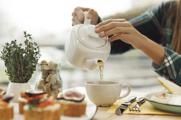 Gros plan vue partielle de la femme versant le thé de la théière pendant le petit déjeuner — Photo de stock