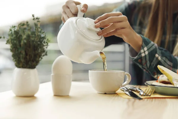 Partial view of girl pouring tea from teapot in cup at breakfast — Stock Photo