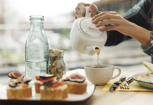 Plan recadré de fille verser le thé de la théière dans la tasse au petit déjeuner — Photo de stock